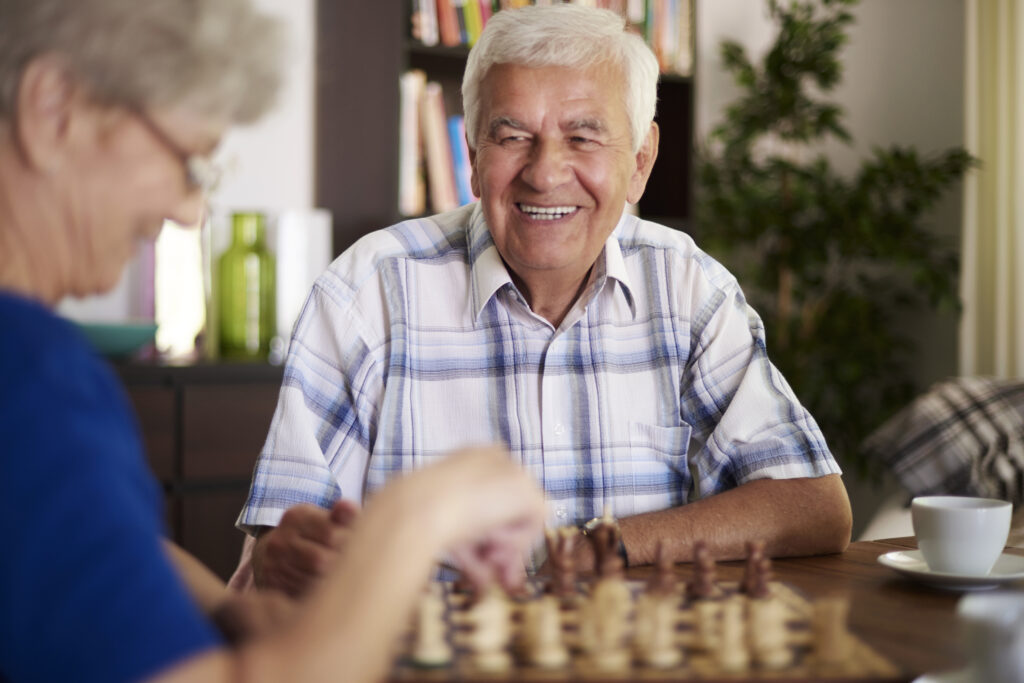 Smiling older man playing chess with a female friend in a cozy indoor setting, representing social engagement in senior living.