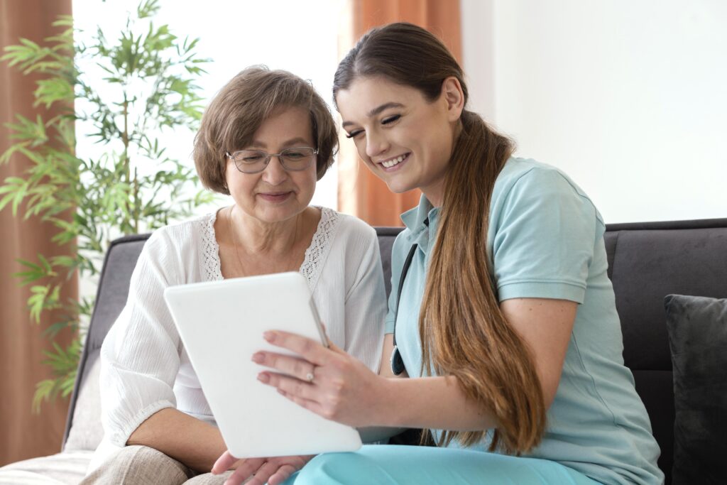 Female caregiver and senior woman smiling while looking at a tablet, highlighting personal support and digital connection in care.